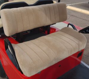 A red golf cart with two seats and beige covers.